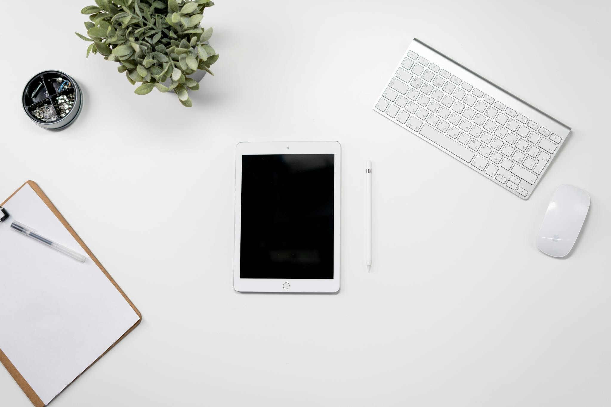 A clean home office desk setup featuring a tablet, keyboard, mouse, and plant for inspiration.