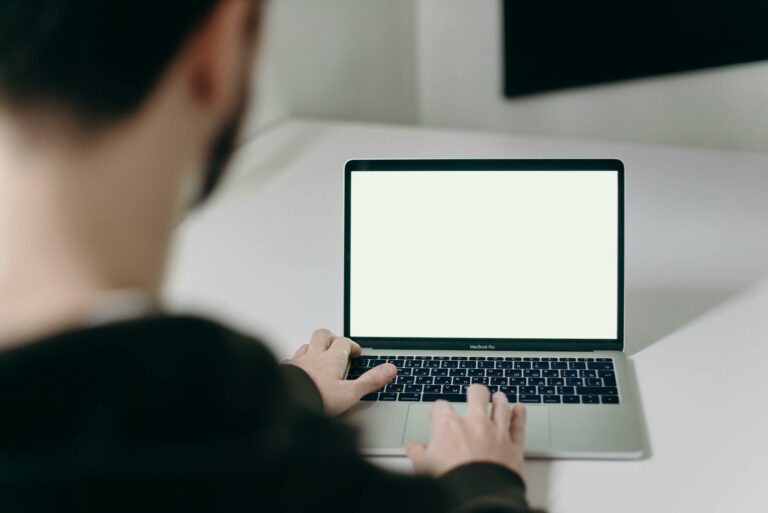 A man in a hoodie works on a blank-screen laptop at a clean, minimalist workspace indoor.