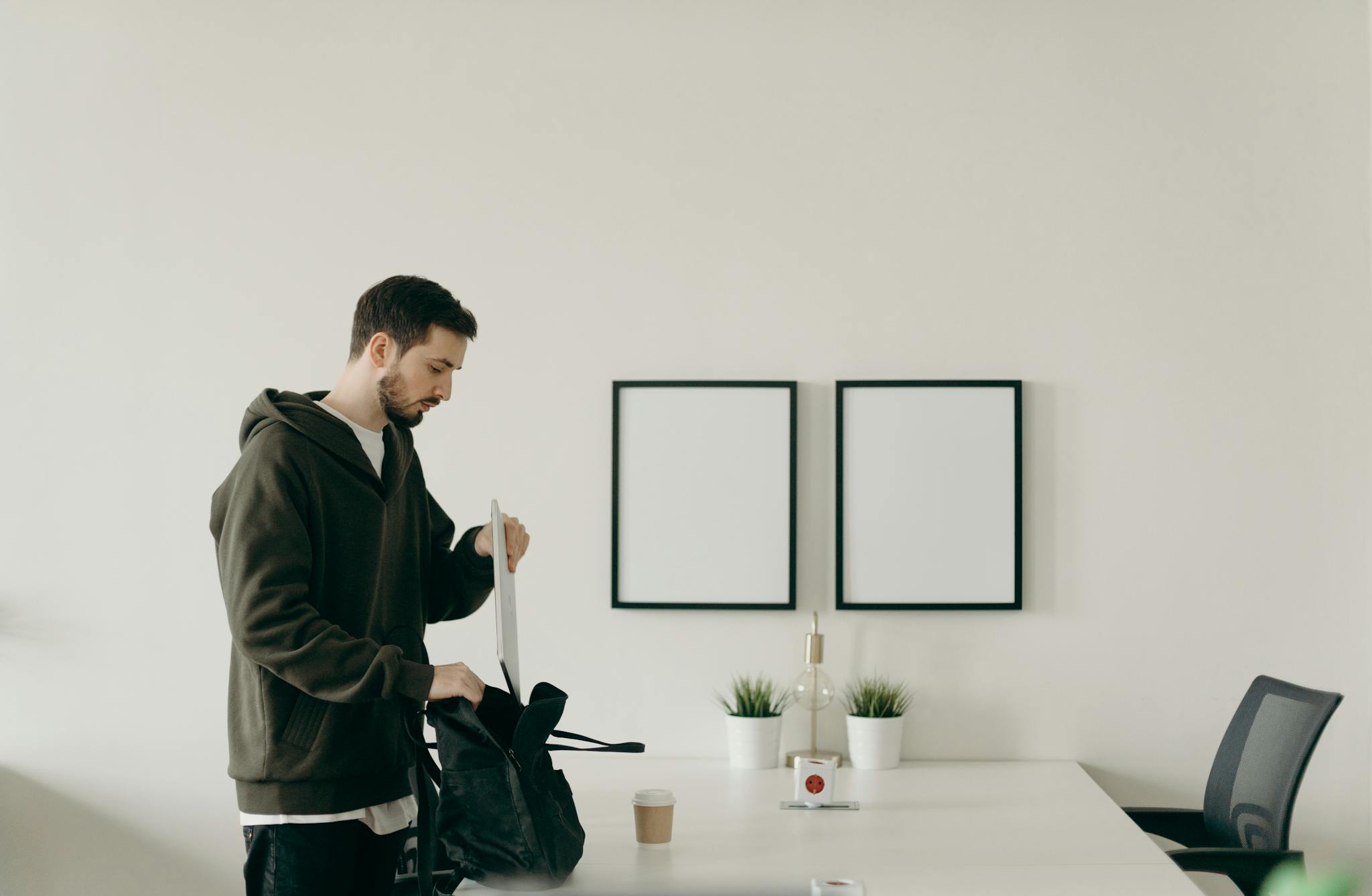 A young man organizing his workspace in a minimalist home office with blank frames.