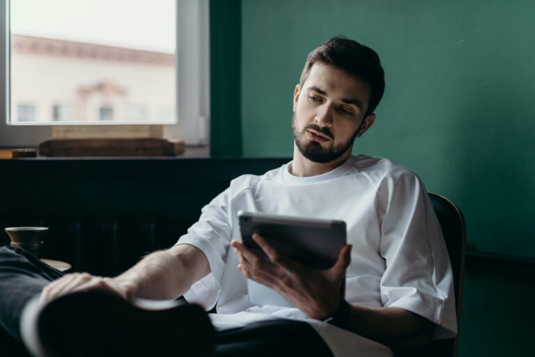 Pensive man using a tablet while relaxing at home. Modern lifestyle concept.