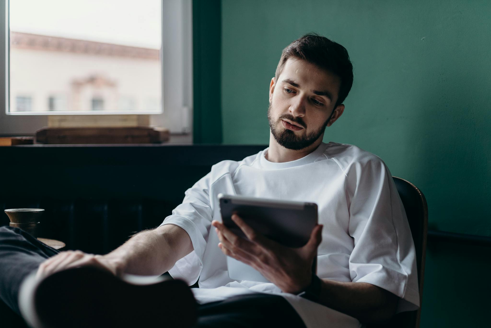 Pensive man using a tablet while relaxing at home. Modern lifestyle concept.